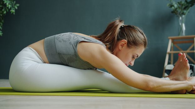 A woman in activewear stretching on a yoga mat indoors, focusing on wellness and fitness.