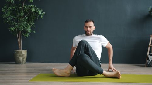 Free A man in a white shirt doing yoga indoors on a green mat, focusing on relaxation. Stock Photo