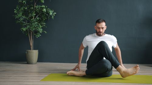 Free Man practicing yoga position on green mat indoors, focusing on flexibility and mindfulness. Stock Photo
