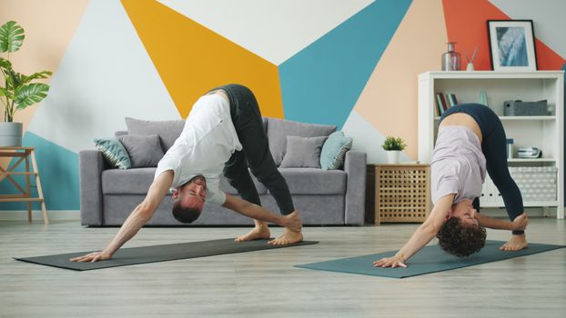 Couple practicing yoga together in a stylish indoor living room with geometric wall design.