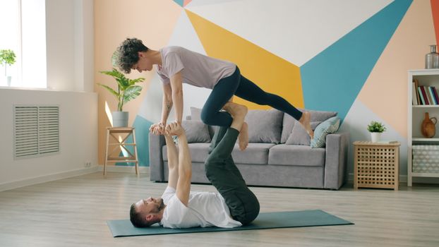 Man and woman performing acro yoga on a mat in a modern living room.