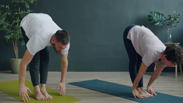 Two individuals performing yoga stretches on mats in a serene indoor setting.
