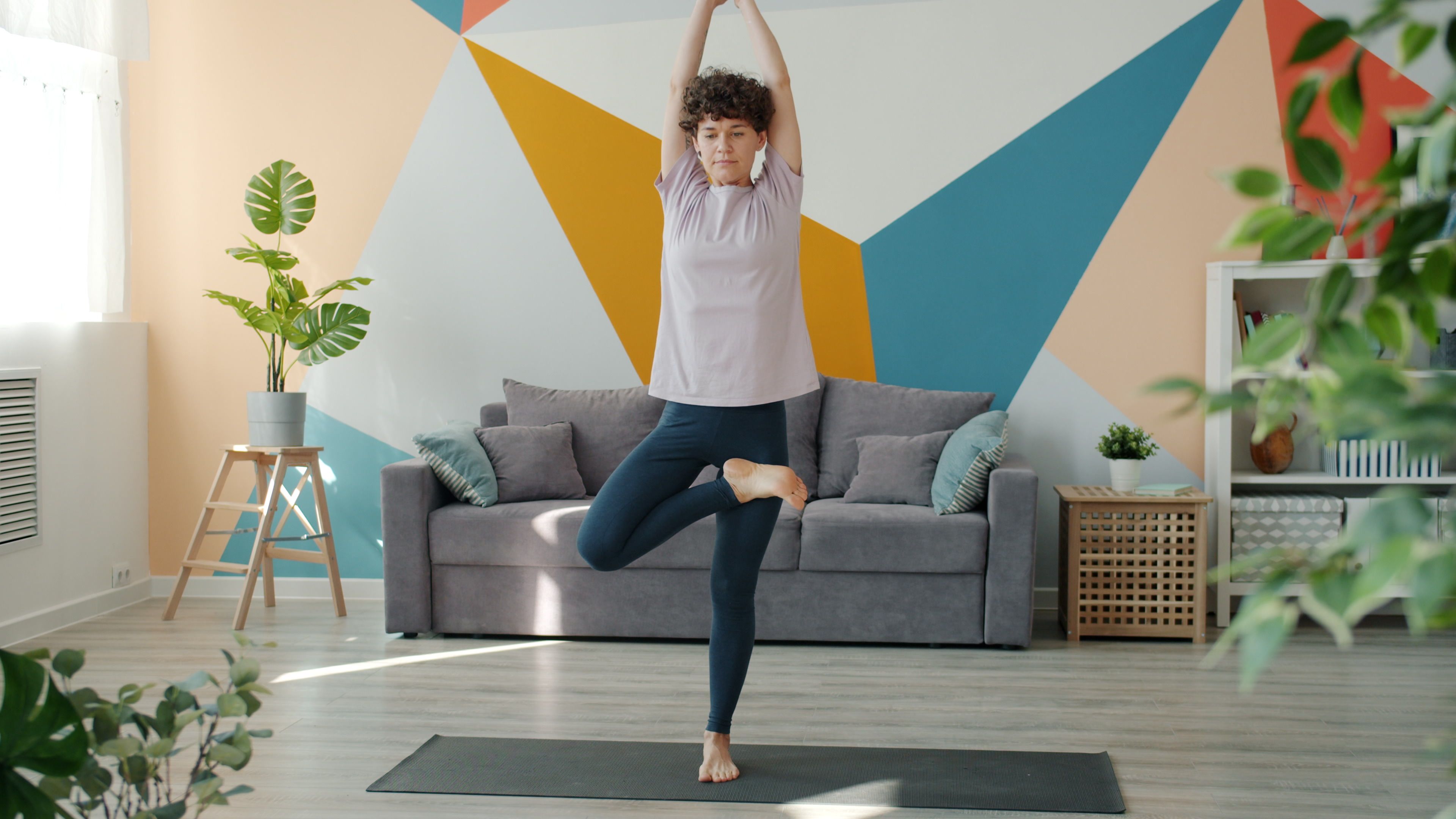 Adult woman doing yoga in a modern, colorful living room with geometric wall design.