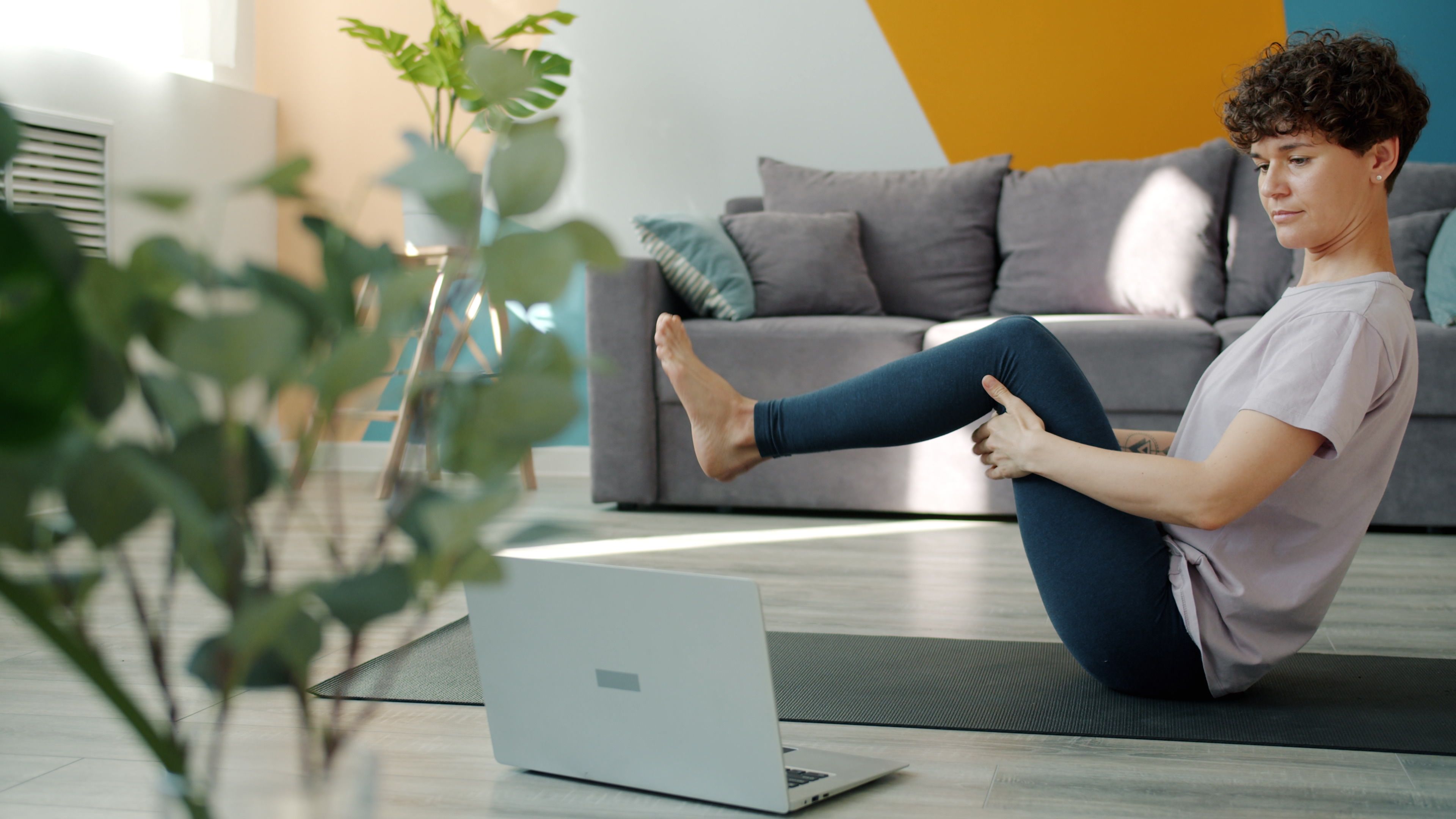 Woman doing yoga at home with focus on laptop. Modern room setting for virtual workout.