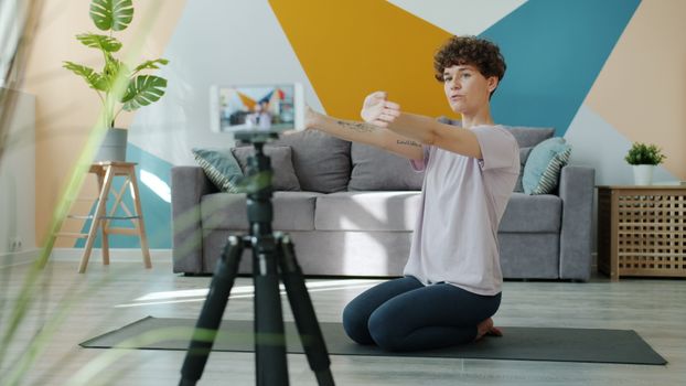 A woman performs yoga stretches at home, recorded with a camera for online content.