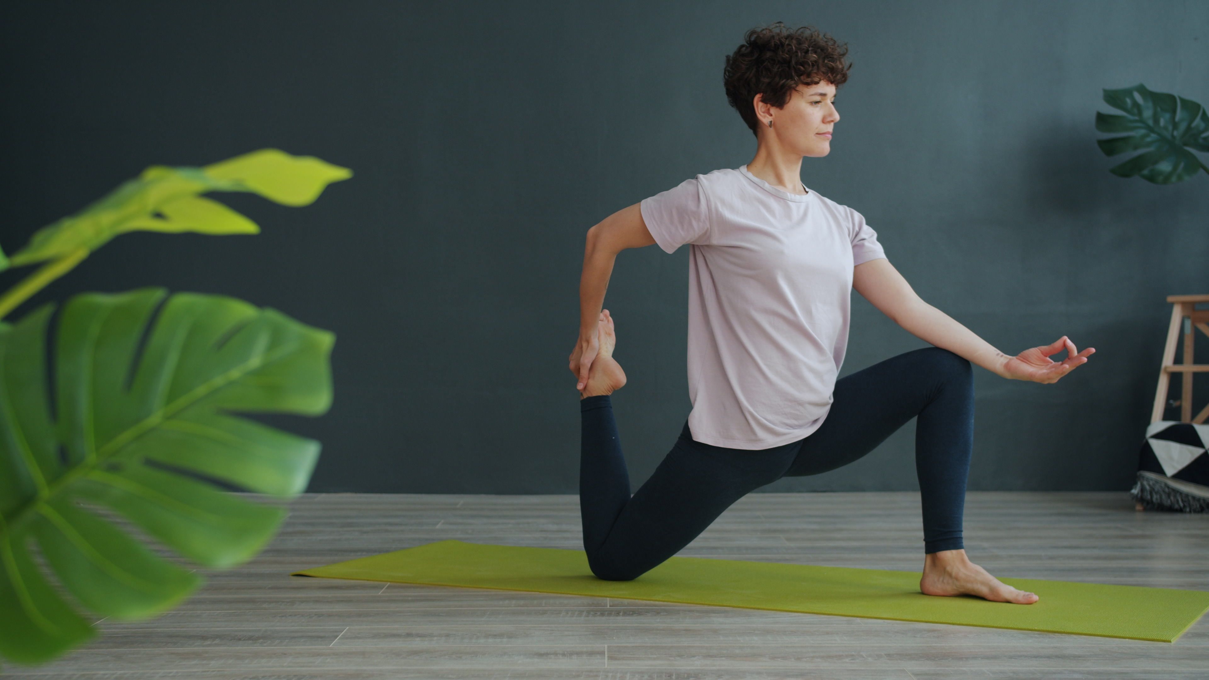 A woman doing a yoga pose on a mat indoors. Calm and focused.