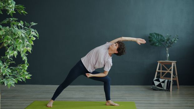 Woman in side stretch yoga pose indoors on a green mat surrounded by plants.
