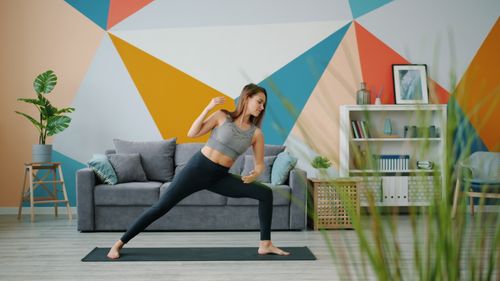 Free Young woman in activewear doing yoga in a colorful, modern living room with geometric wall art. Stock Photo