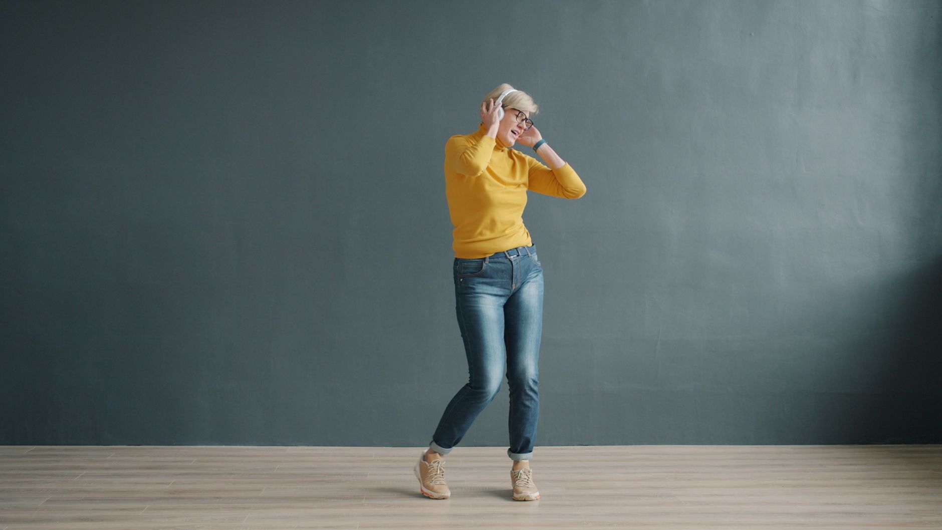 Woman joyfully dancing in casual attire listening to music indoors.