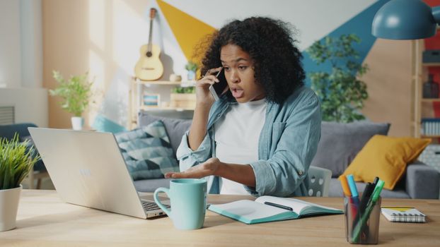 Young woman multitasking in home office environment using laptop and phone.