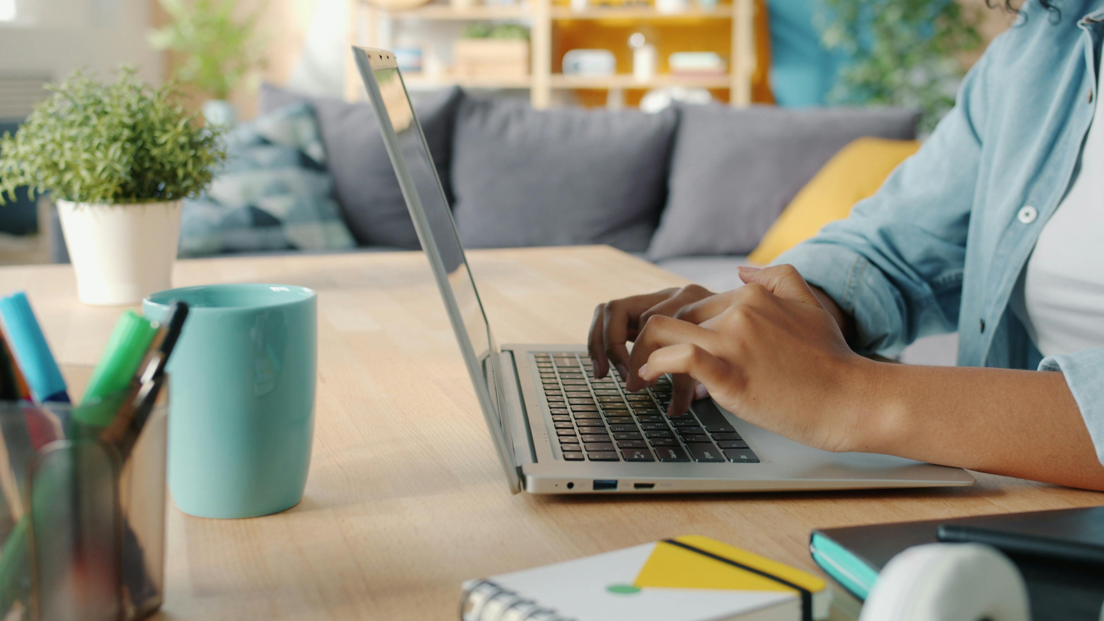 Close-up of a woman typing on a laptop in a cozy home office environment.