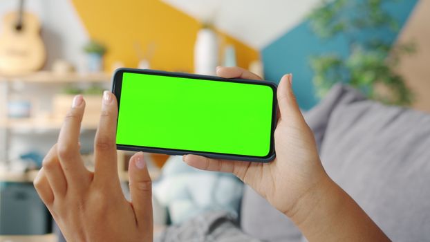Close-up of hands holding a smartphone with a green screen in a colorful room.