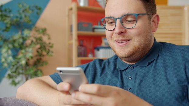 Smiling man wearing glasses and using a smartphone at home.