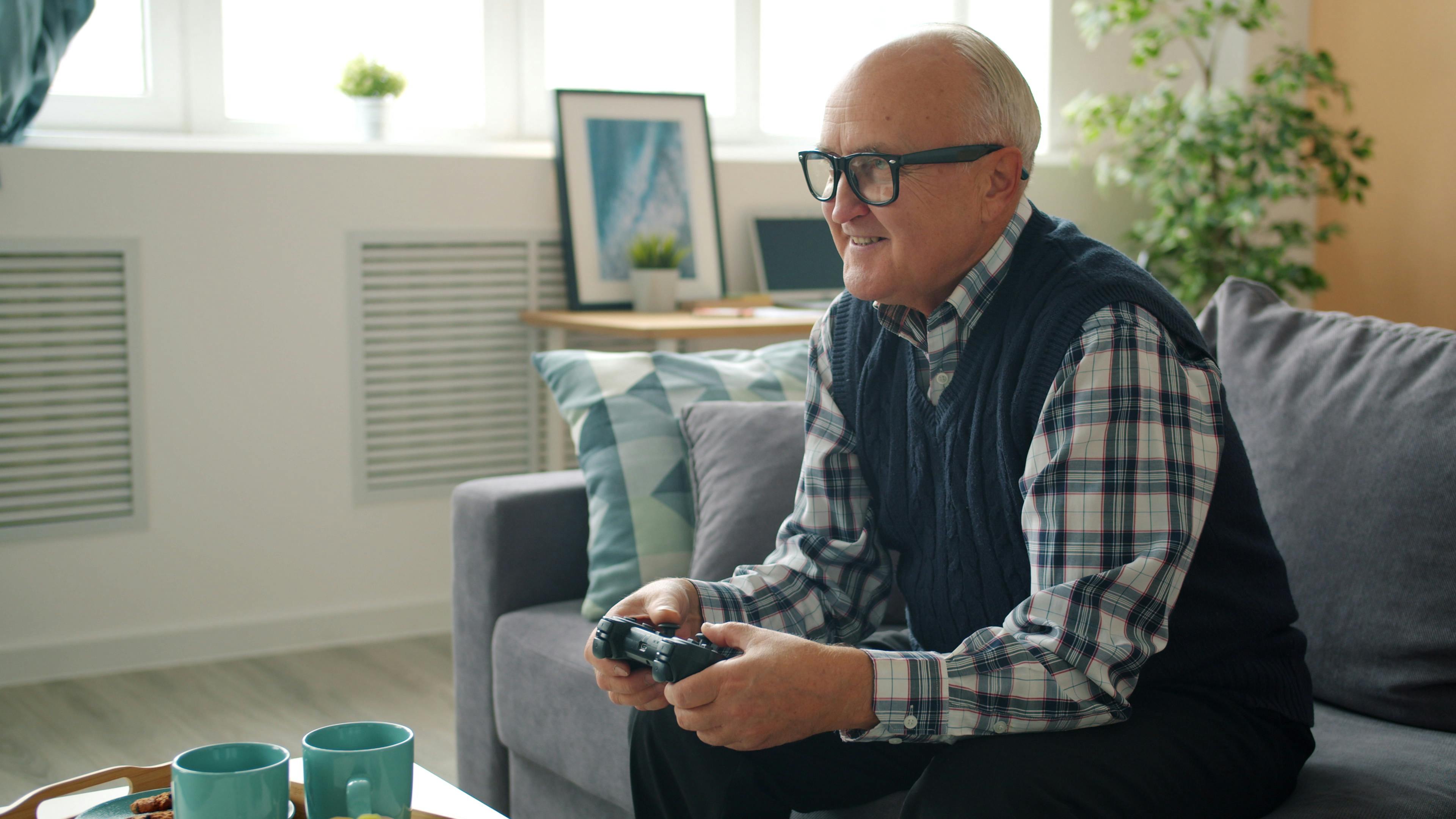 Elderly man playing video games on a console in a cozy living room setting.