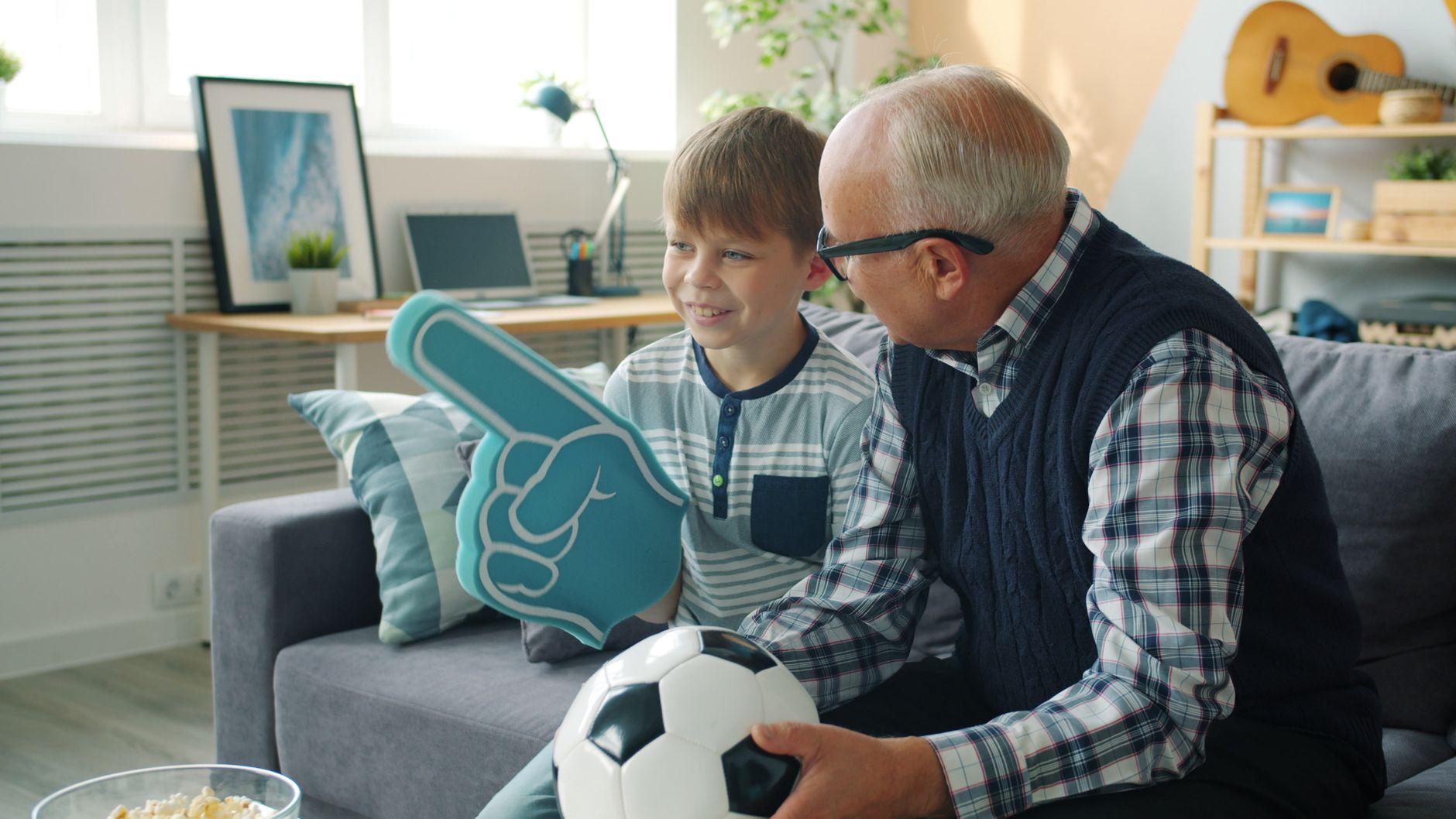 A grandfather and grandson bonding over soccer with foam finger indoors.