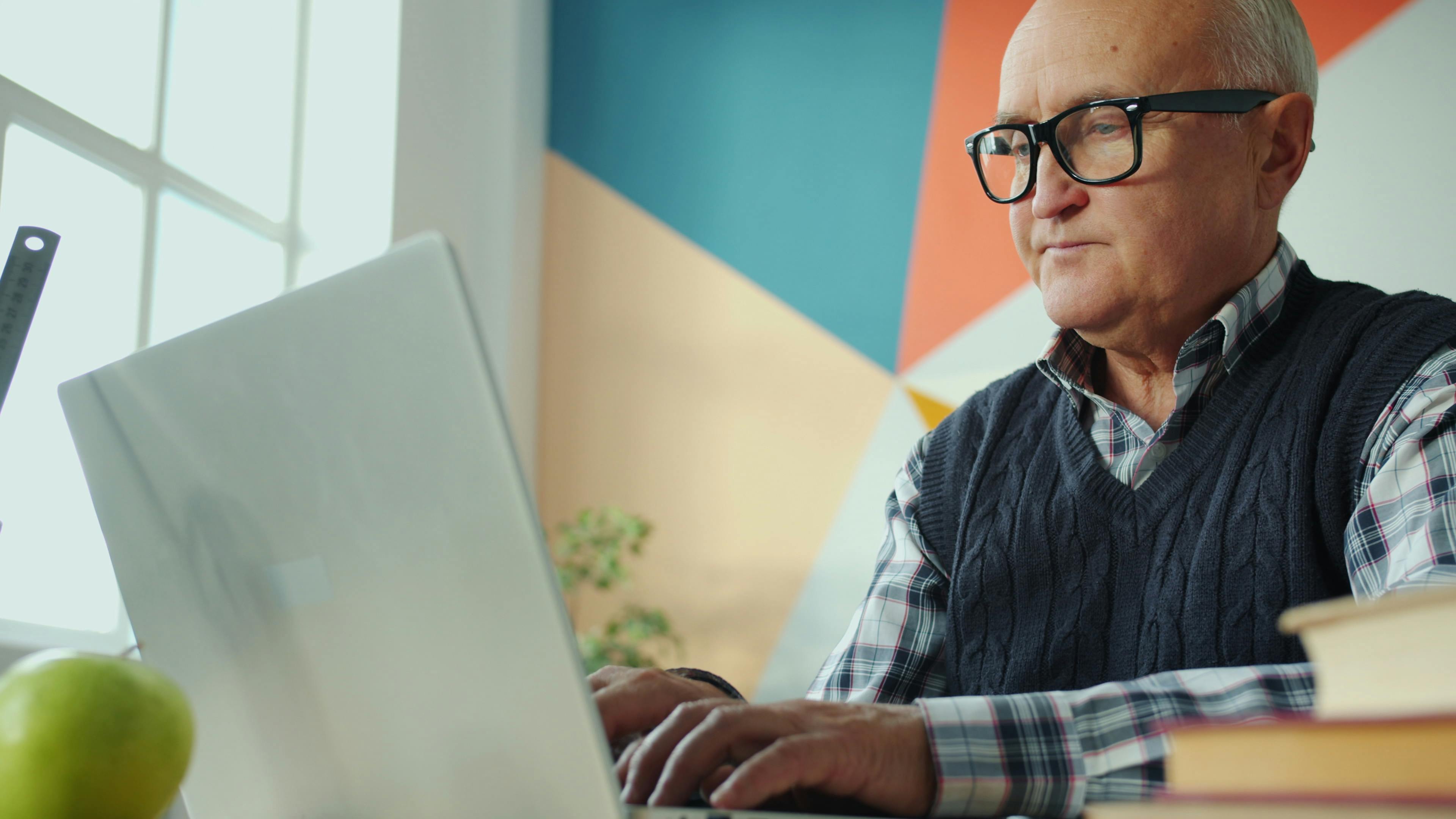 Elderly man focused on his laptop in a stylish, colorful office environment.