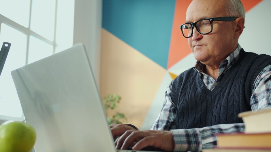 Withings ScanWatch 2 vs Apple Watch: Health Monitoring Showdown (2024) Elderly man focused on his laptop in a stylish, colorful office environment.