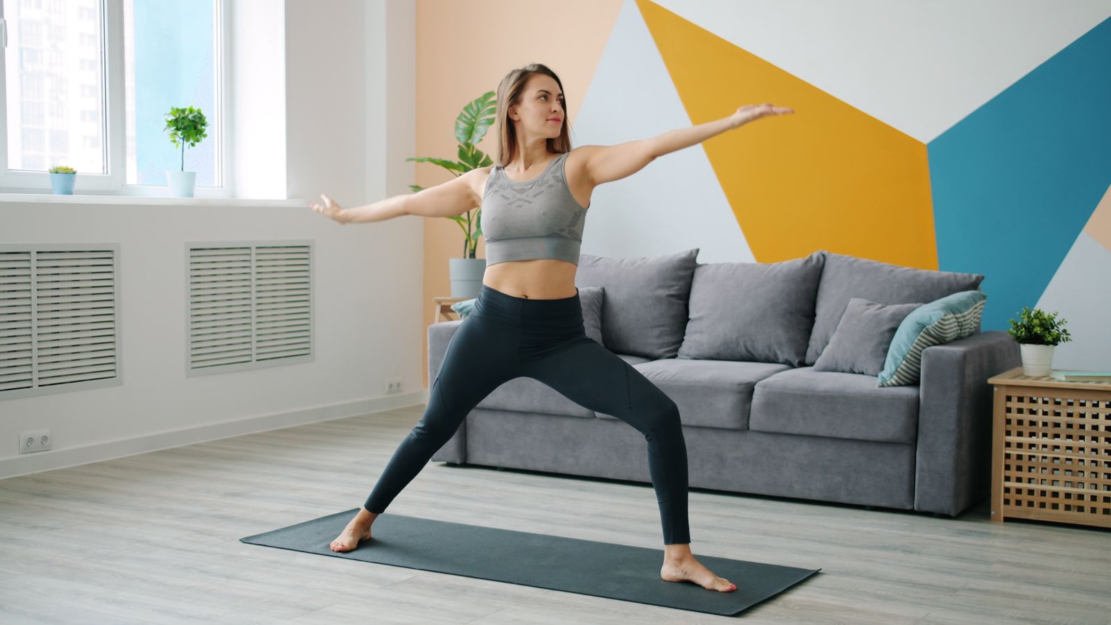 Woman in activewear practicing a yoga stretch in a bright living room as part of a home routine