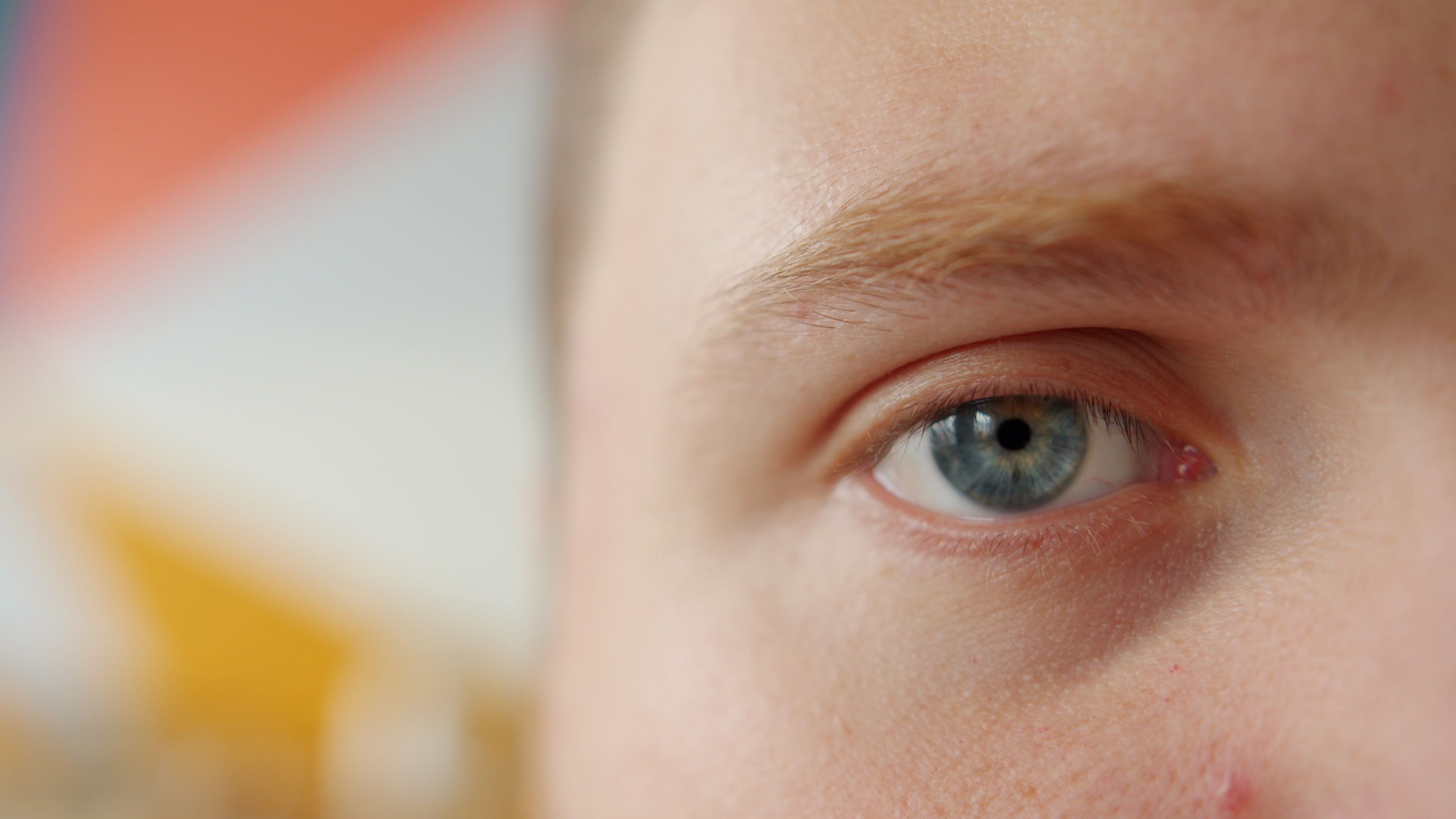 Detailed close-up of a blue eye with a colorful blurred background, emphasizing detail.