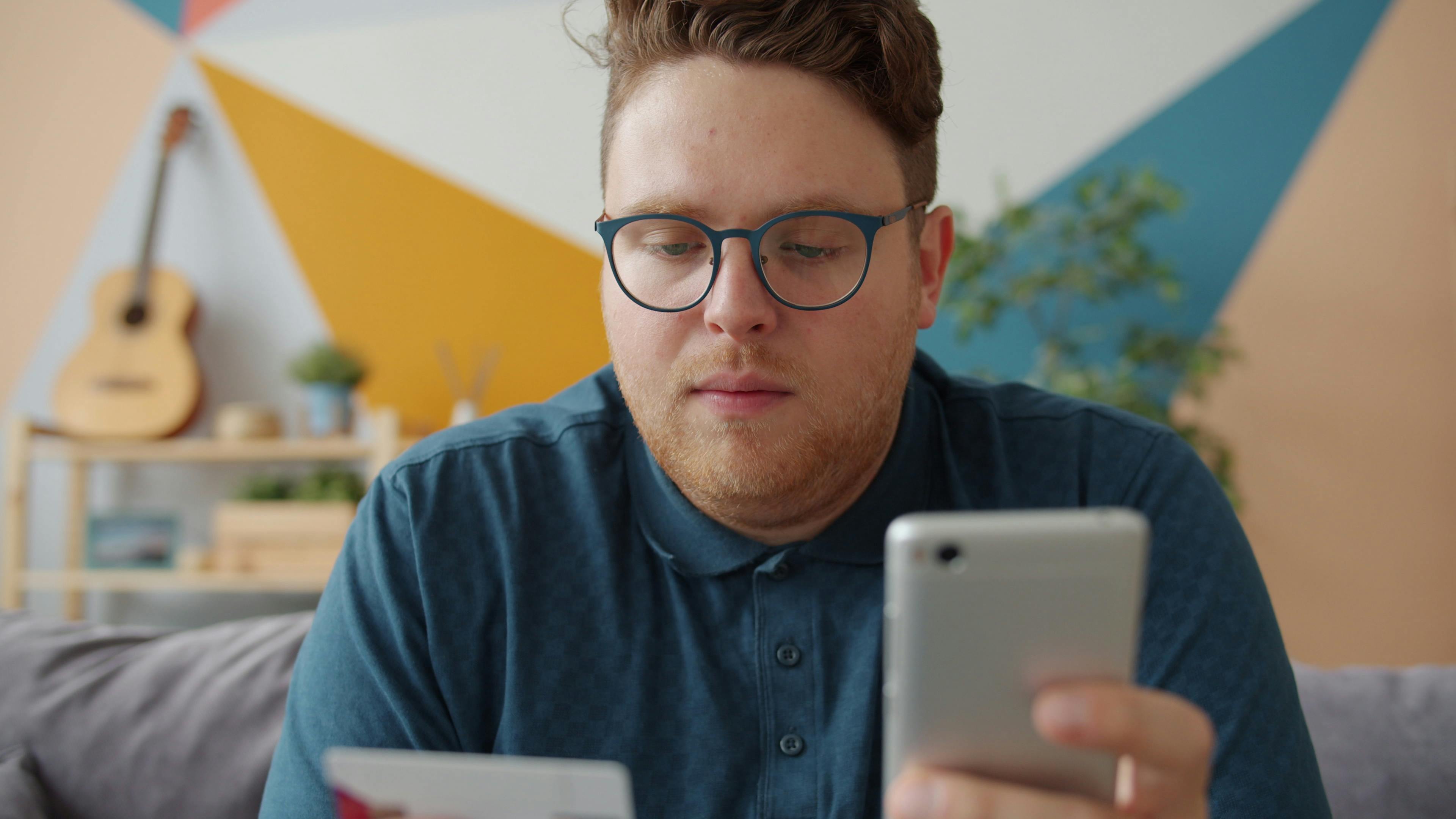 Adult man using smartphone and credit card for online shopping in modern living room.