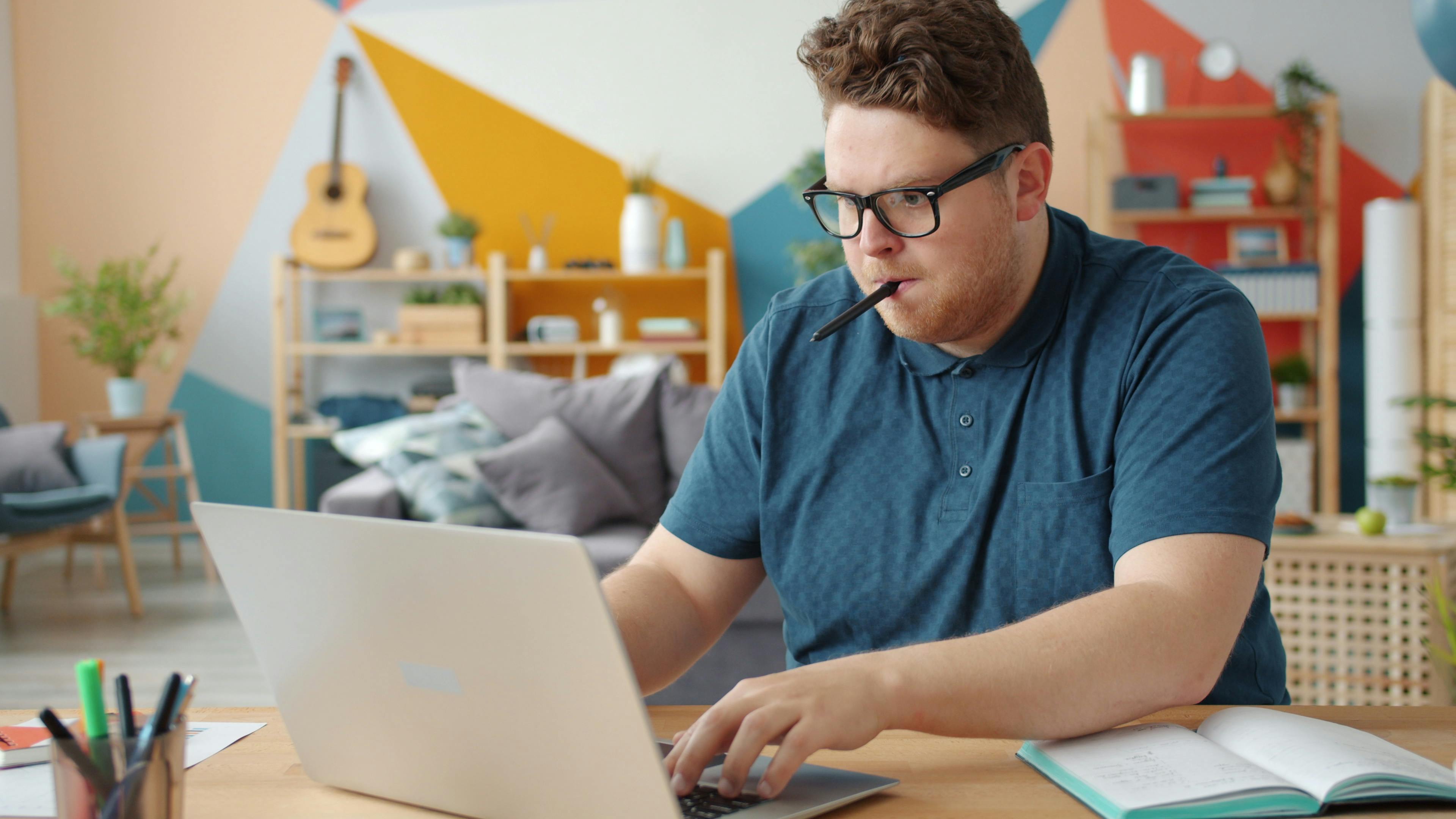 Young man focusing intently while working on a laptop in a stylish home office.