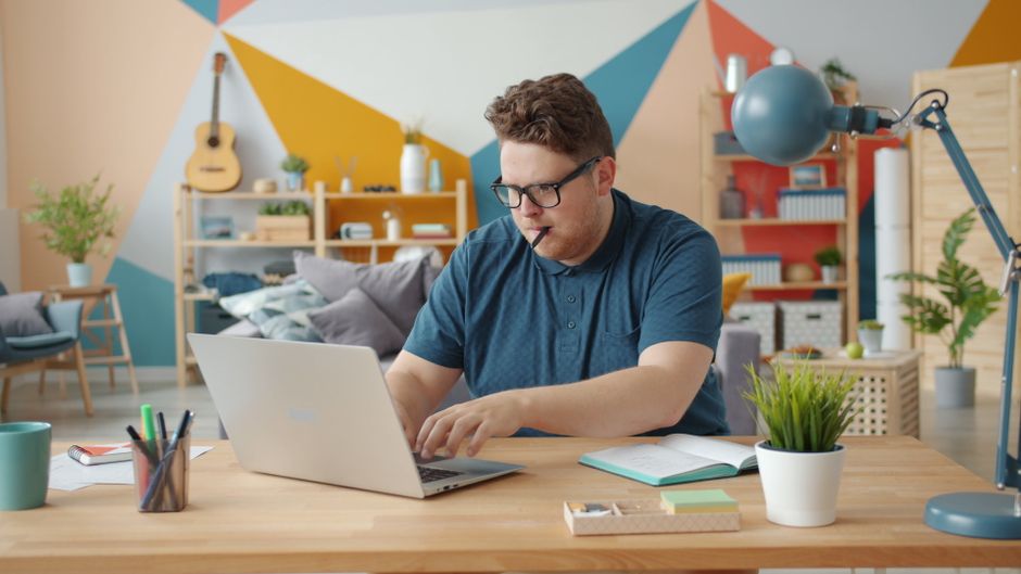 Policygenius vs Zander Insurance: Life Insurance Quotes Face-Off A young man focused on his laptop at a stylish home office with a colorful geometric wall.