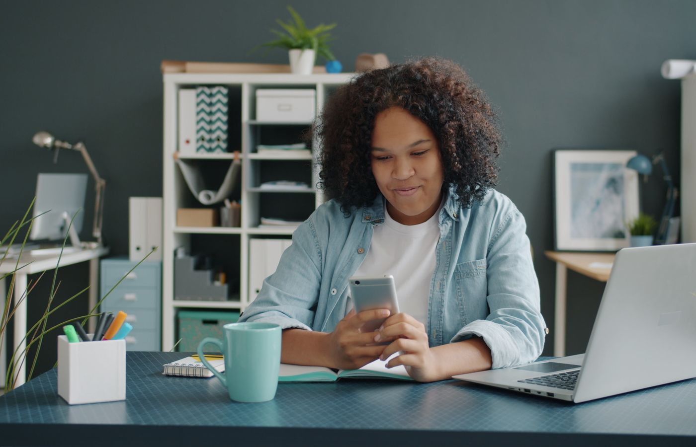 Young woman working in a modern office setting, actively using a smartphone at her desk.