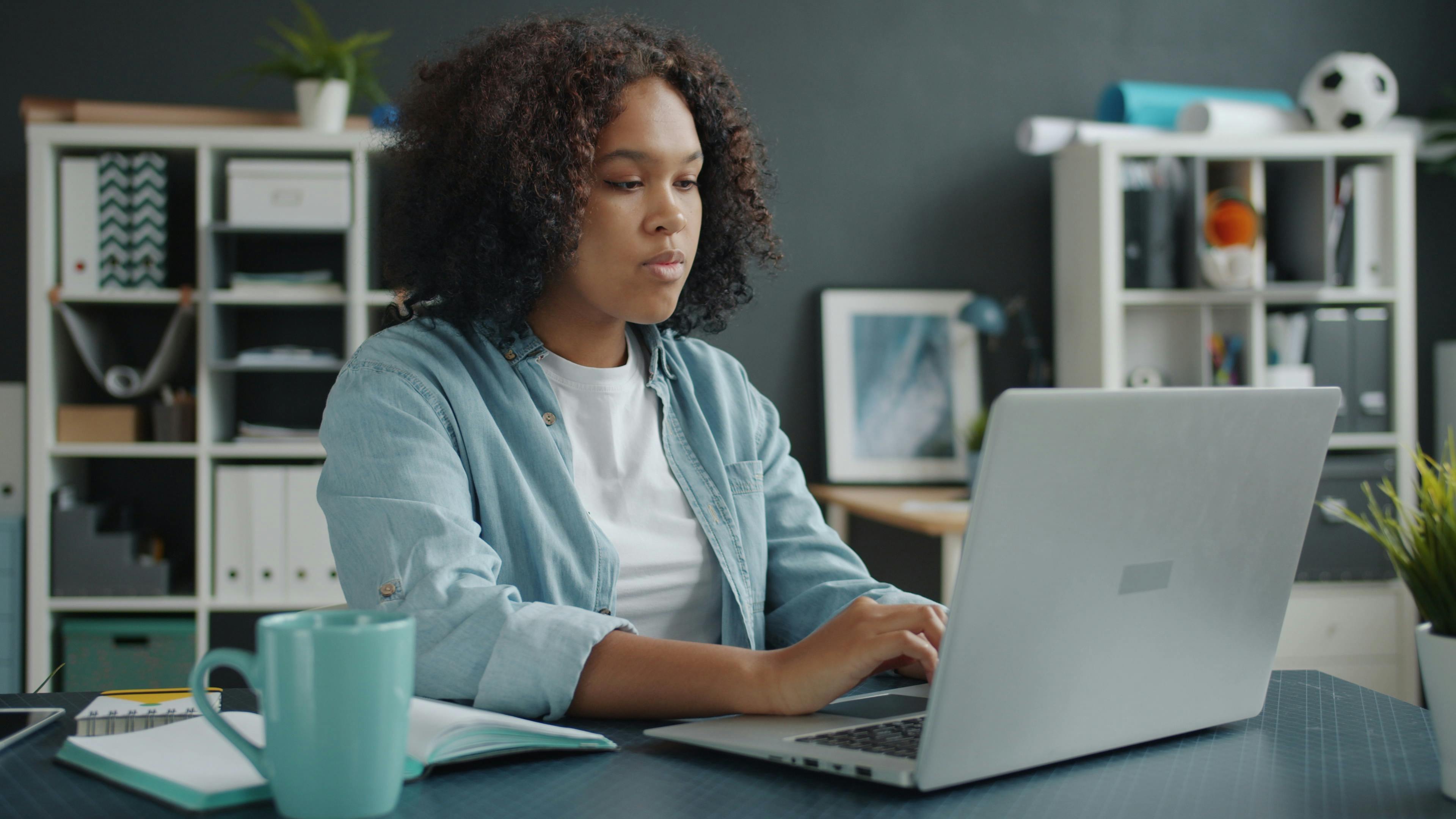 Young woman focused on remote work at home office desk with laptop.