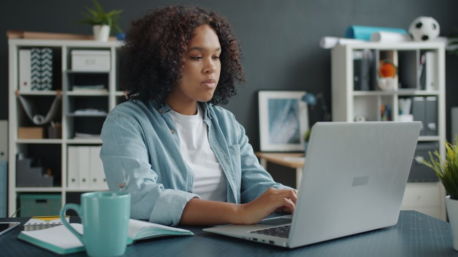 Como Criar um Espaço de Trabalho Inspirador e Funcional 2 Young woman focused on remote work at home office desk with laptop.