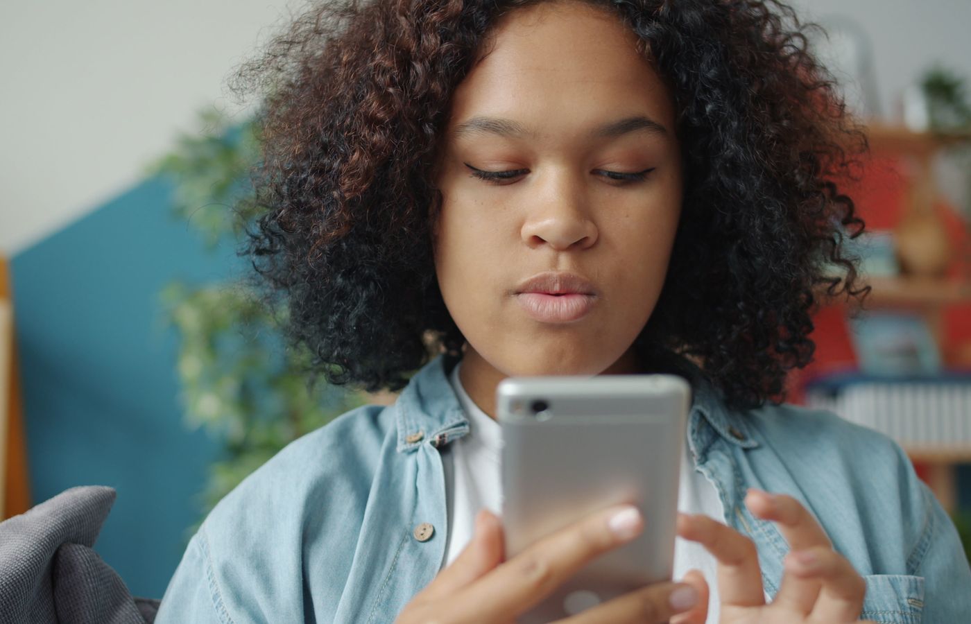 Teenage girl focused on her smartphone at home, with a cozy indoor background.