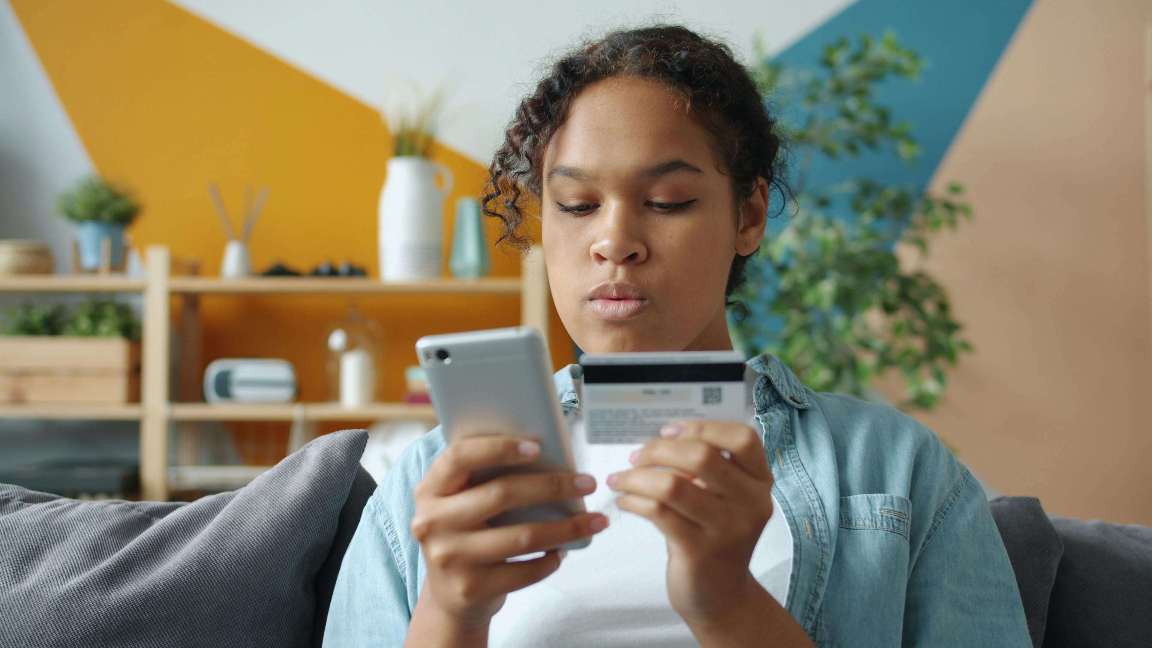 Young woman using smartphone and credit card for online shopping at home.