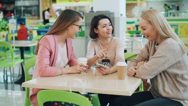 Three friends laughing and enjoying coffee together indoors.