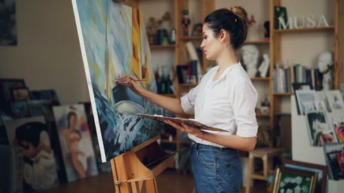 Free Young female artist painting a vibrant ocean scene in her art studio. Stock Photo