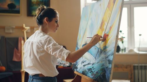 Free Young female artist painting a colorful seascape on canvas indoors. Stock Photo