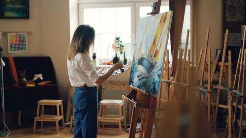 Free Female artist painting a vibrant sailboat in a well-lit studio. Stock Photo