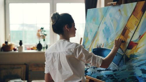 Free Side view of a woman painting a colorful abstract artwork on a canvas in a studio. Stock Photo
