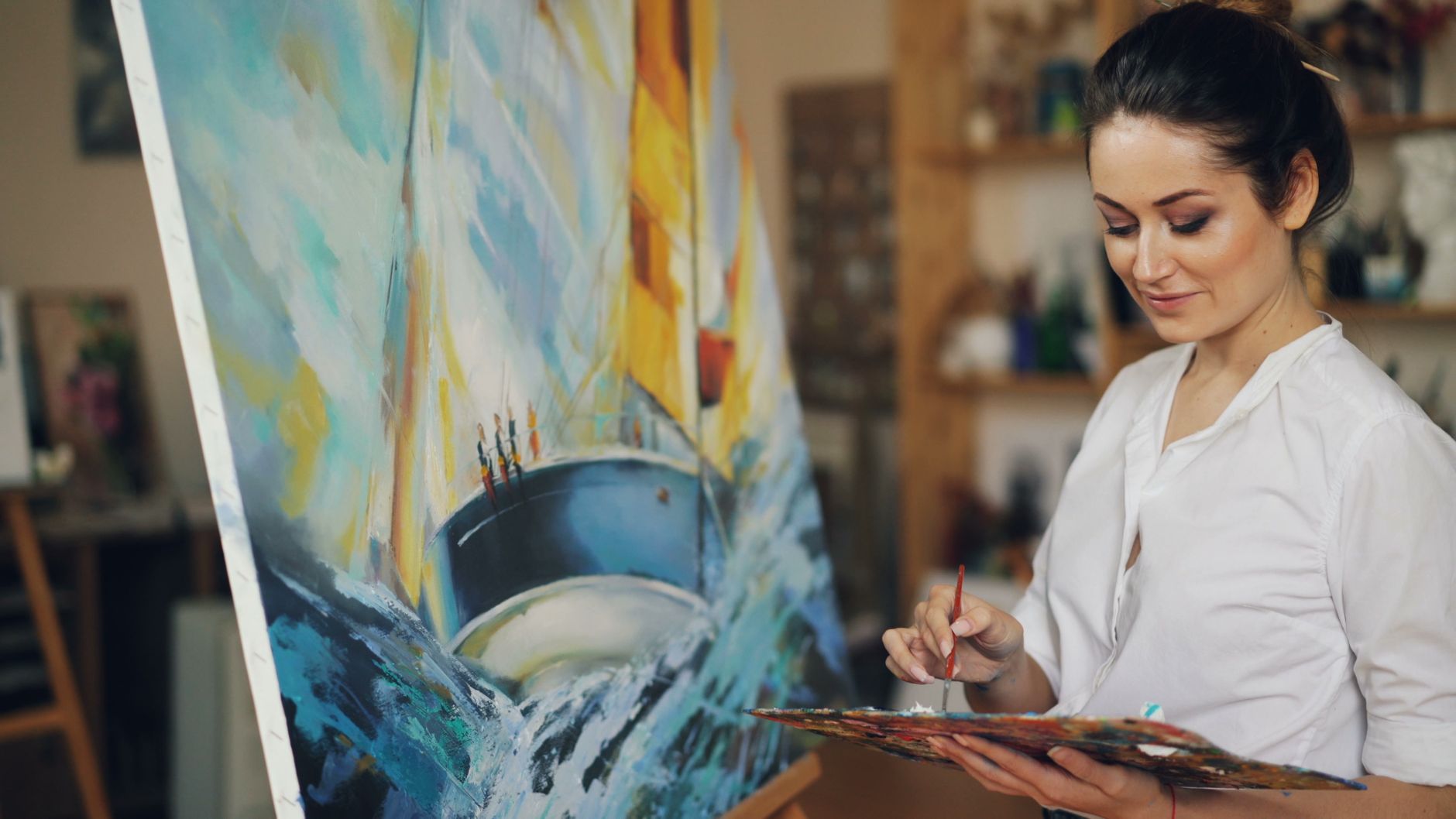 Artist painting a vibrant sailboat scene on canvas indoors.