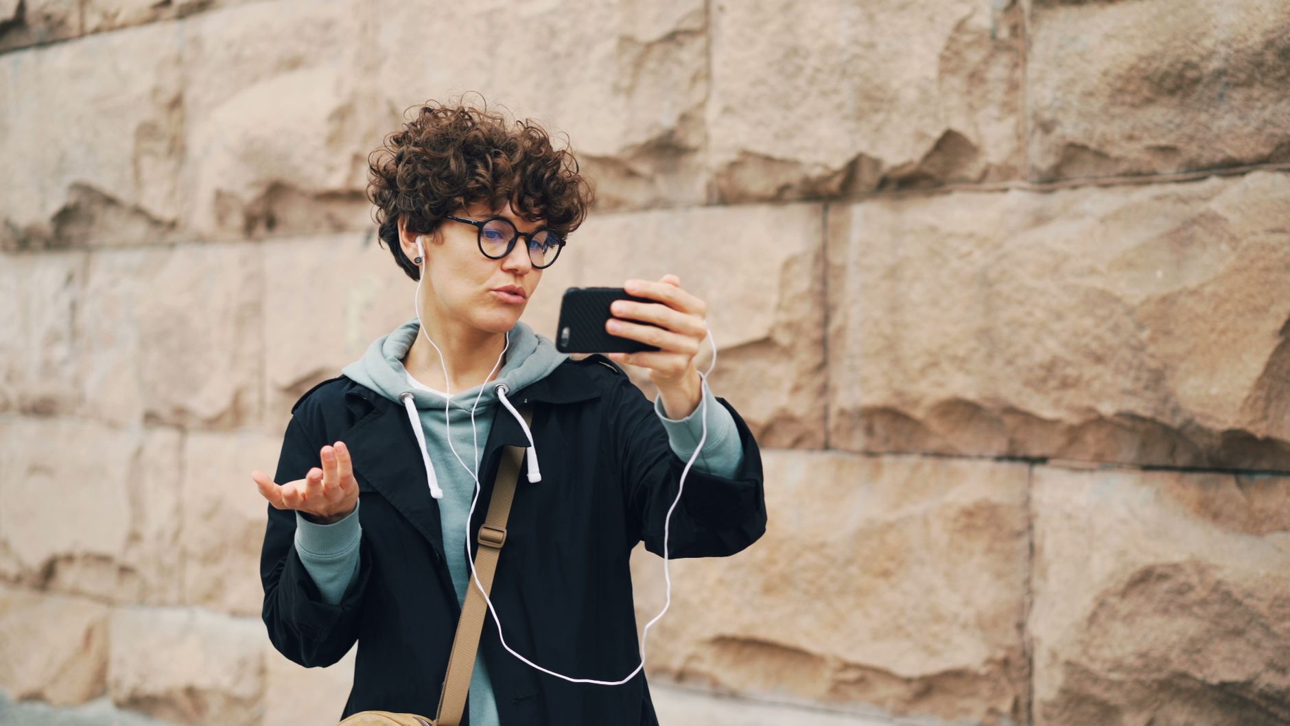 Casual young adult taking a selfie with smartphone against stone wall.