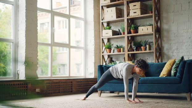Woman doing yoga indoors in a bright, plant-filled living room.