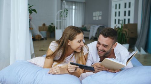 Free Smiling couple reading together on a bed, enjoying a relaxing day indoors. Stock Photo