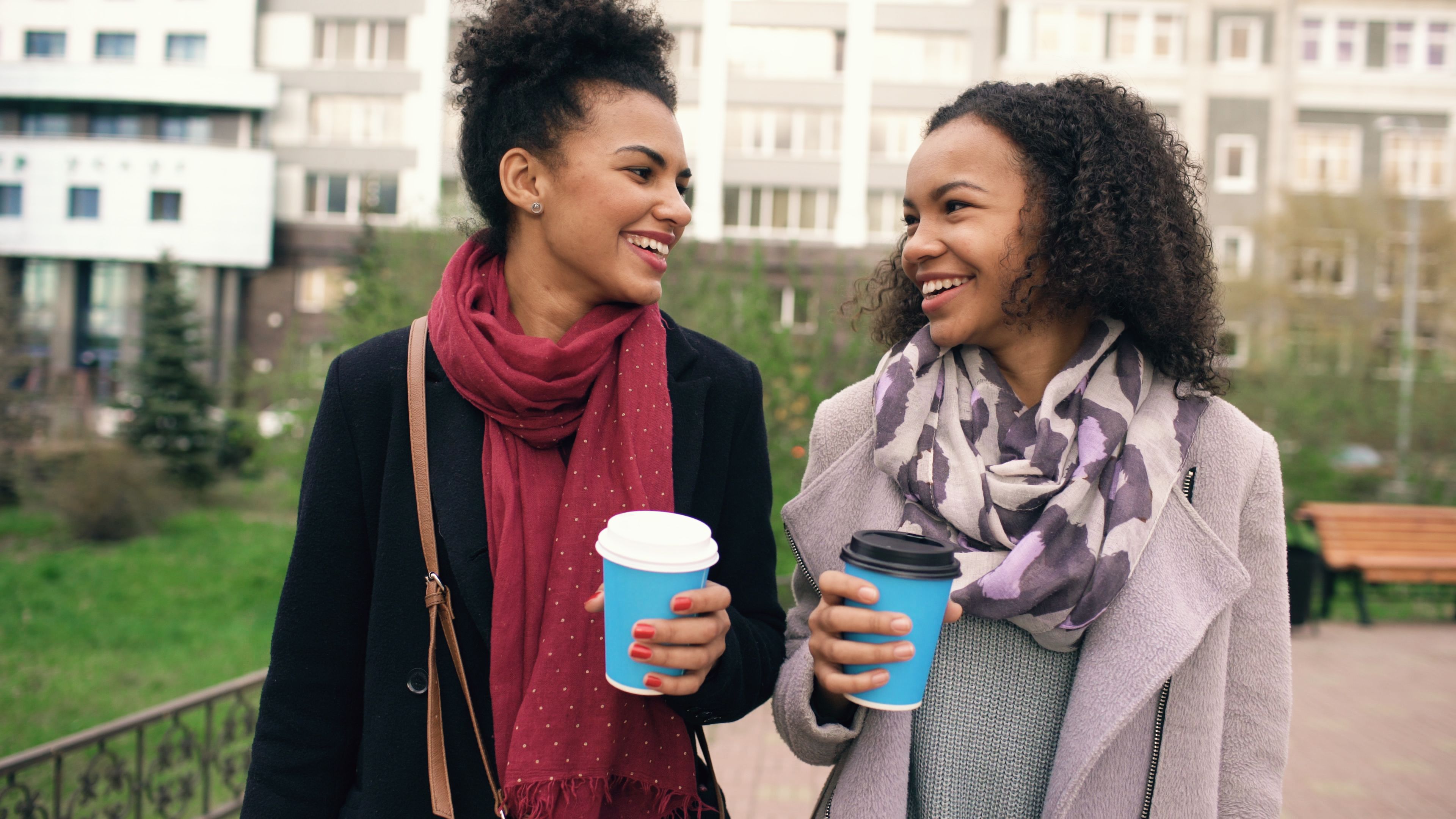 Two women laughing and enjoying coffee together outdoors.
