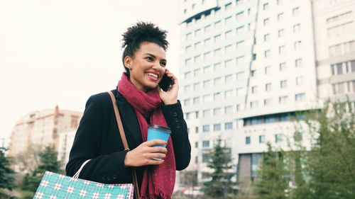 Free Smiling woman in urban setting talking on mobile, holding coffee. Stock Photo
