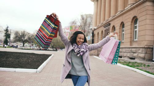 Free Happy woman holding shopping bags in city on a cool day. Stock Photo