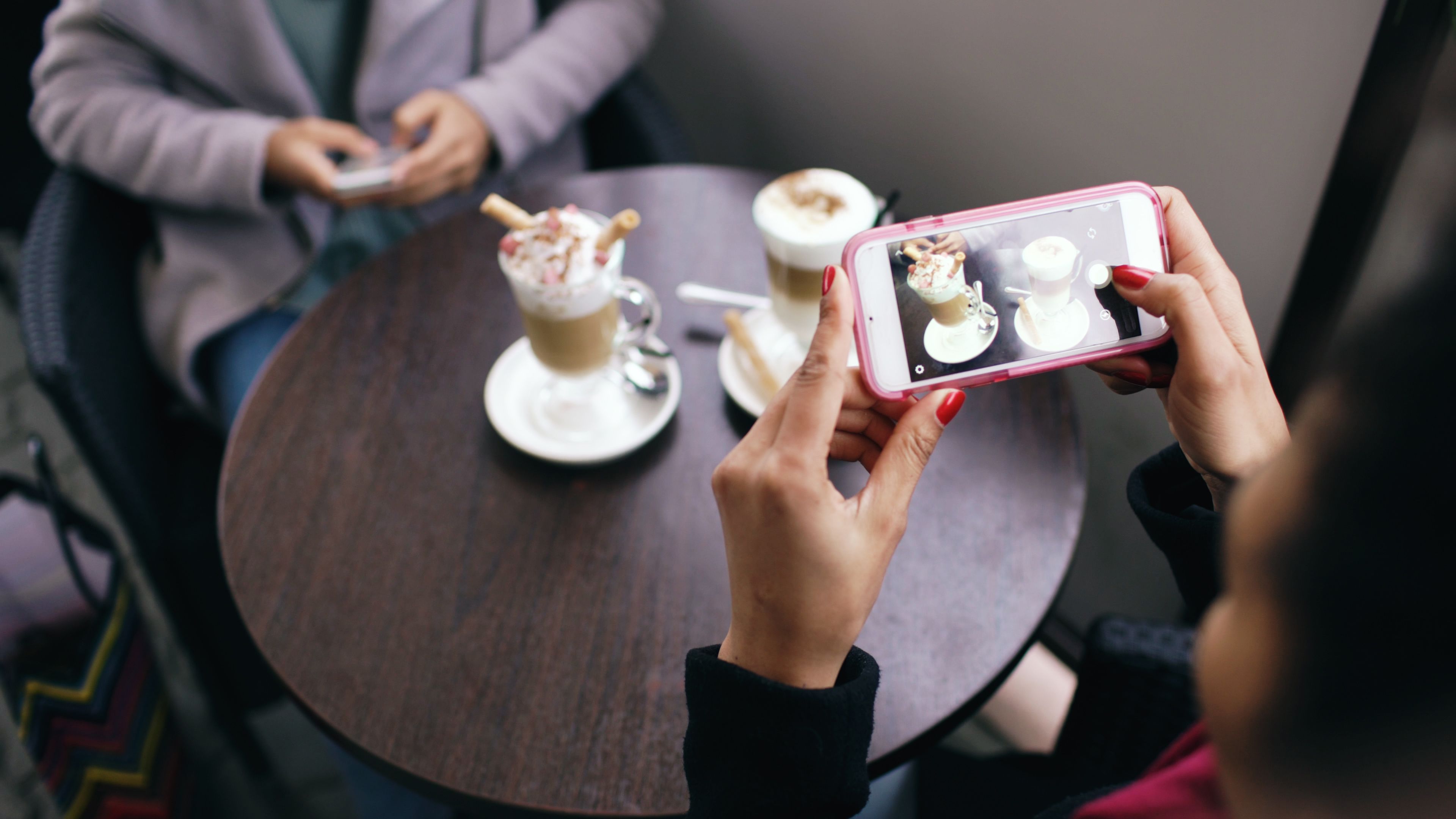 Two women in a cafe capturing photos of their coffee with smartphones.