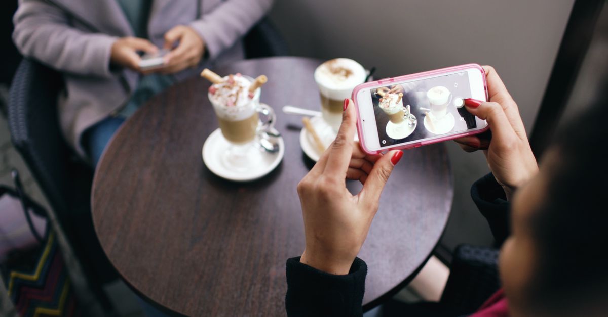 Two women in a cafe capturing photos of their coffee with smartphones.