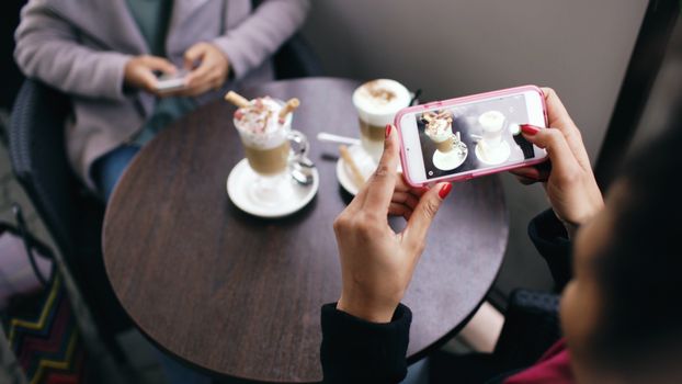 Two women in a cafe capturing photos of their coffee with smartphones.