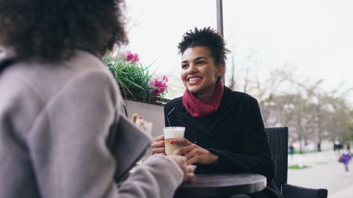 Free Two women enjoying a friendly chat at an outdoor café with coffee drinks. Stock Photo