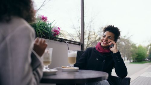 Free A joyful woman chats on the phone while enjoying coffee outdoors. Stock Photo