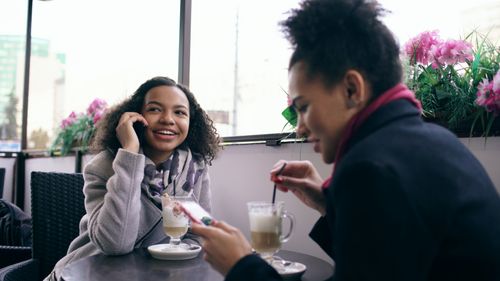 Free Two women chatting and having coffee in a cozy cafe setting with pink flowers. Stock Photo