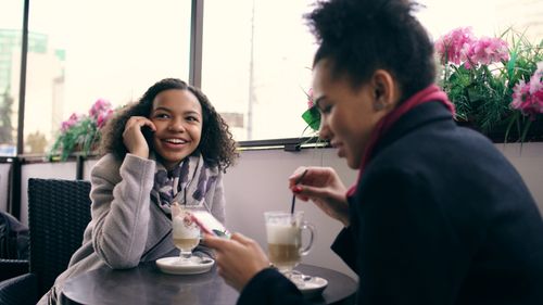 Free Two women sitting at a café table enjoying drinks and chatting. Stock Photo